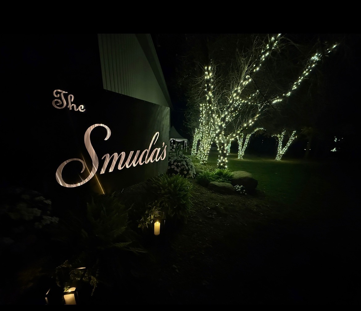 Personalized illuminated wedding sign beside trees wrapped in warm string lights