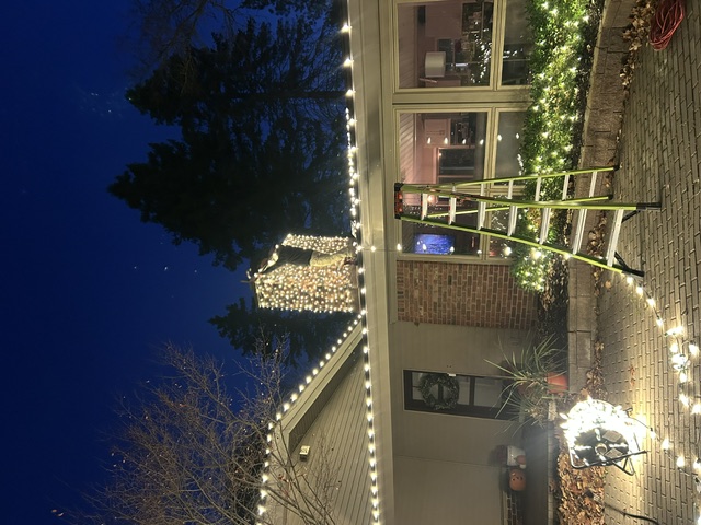 LuxeGlow technician wrapping a home chimney in lights from a ladder