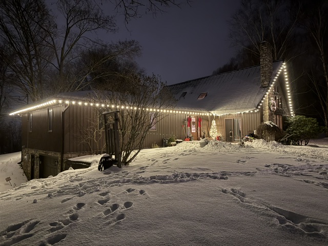 Dark siding home with roofline lighting and lit stone chimney at dusk